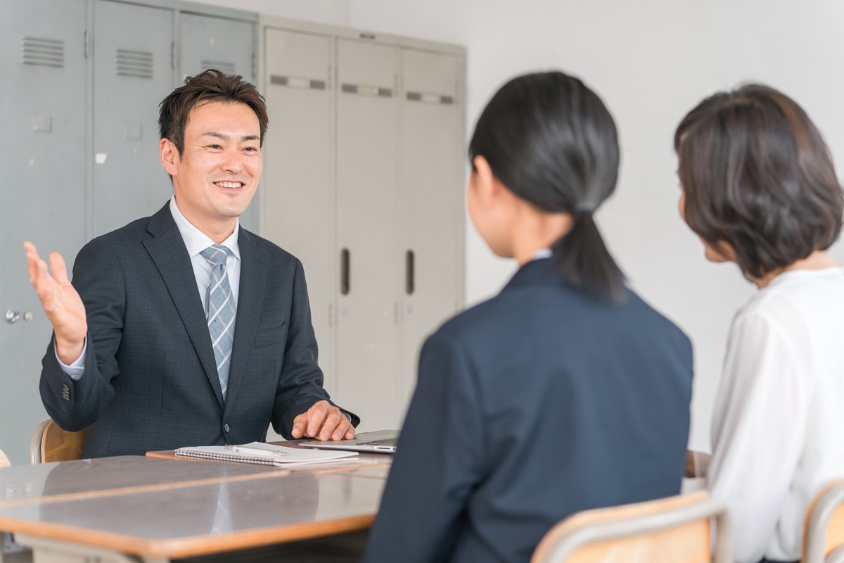 先生と保護者、高校生が学校で相談する様子