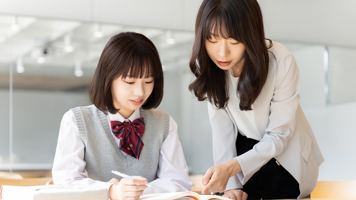 机で教材を見ながら学ぶ生徒と、隣で説明する大人